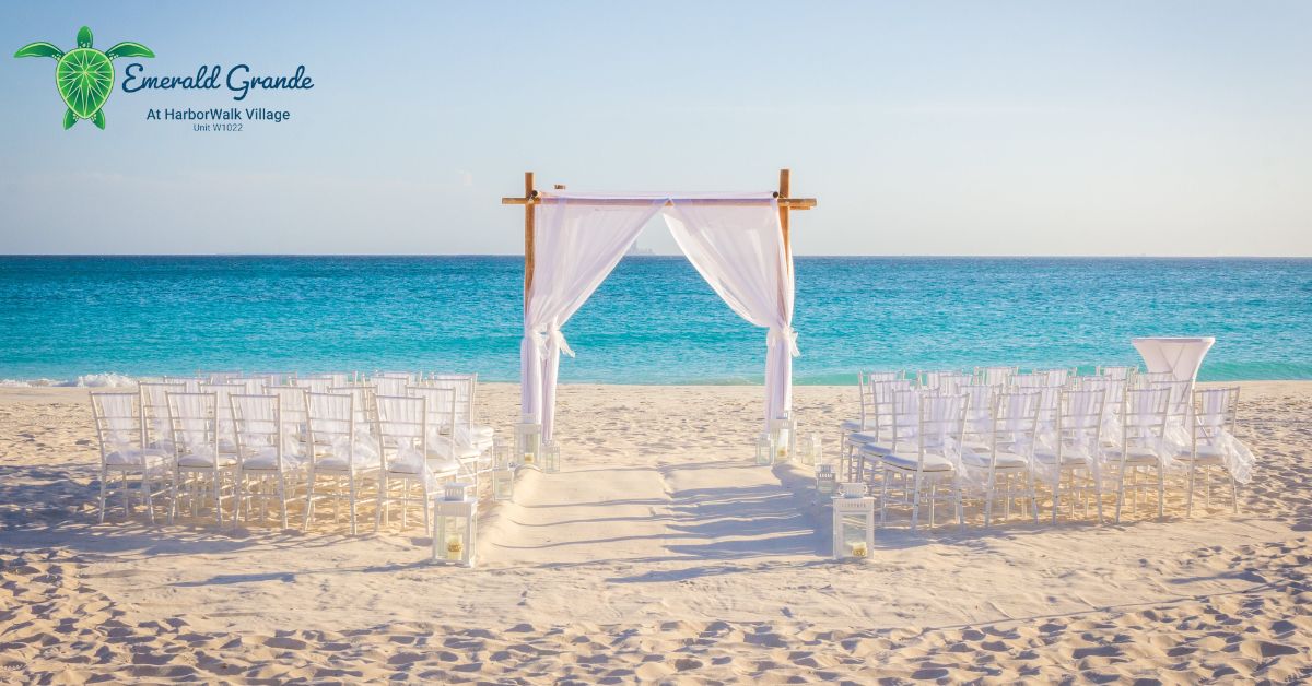 Beach wedding ceremony setup at Emerald Grande in Destin with white chairs, draped arch and Gulf backdrop